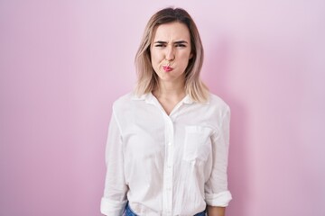 Young beautiful woman standing over pink background puffing cheeks with funny face. mouth inflated...