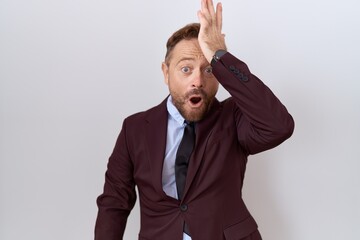 Middle age business man with beard wearing suit and tie surprised with hand on head for mistake,...