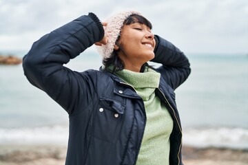 Young beautiful hispanic woman smiling confident relaxed with hands on head at seaside
