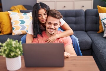 Man and woman couple using laptop sitting on sofa at home