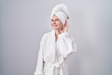 Blonde caucasian woman wearing bathrobe smiling with hand over ear listening an hearing to rumor or gossip. deafness concept.