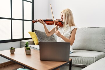 Young blonde woman musician smiling confident having online violin lesson at home