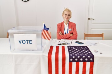 Young blonde woman electoral table president sitting on table with arms crossed gesture at...
