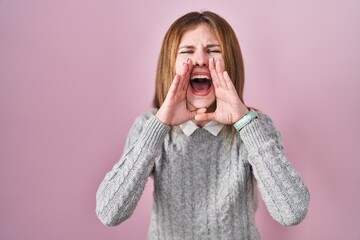 Beautiful woman standing over pink background shouting angry out loud with hands over mouth