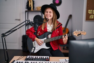 Young blonde woman musician singing song playing electrical guitar at music studio