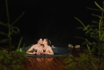 Couple enjoying hot tub at night outdoors. Winter holidays in mountains, hot water treatments...