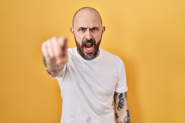 Obraz premium Young hispanic man with tattoos standing over yellow background pointing displeased and frustrated to the camera, angry and furious with you