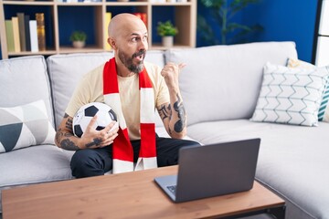 Hispanic man with tattoos watching football match hooligan holding ball on the laptop pointing...