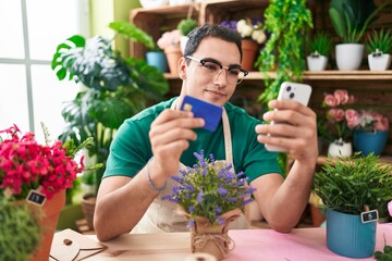 Young hispanic man florist using smartphone holding credit card at flower shop