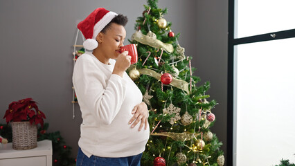 Obraz na płótnie Canvas Young pregnant woman celebrating christmas smelling cup of coffee at home