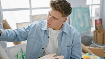 Handsome bearded young caucasian man, an artist, concentrated and immersed in his craft, sits drawing in art class at the university studio, creating magic on canvas.