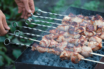 Cooking pork barbecue. Male hands turns skewers with meat.