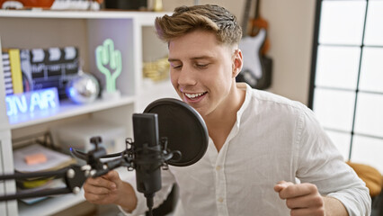 Smiling young caucasian man joyfully belting out a song in the cozy ambiance of a music studio.