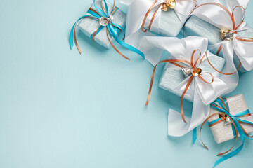 Gift boxes wrapped in blue, white and silver paper with white, blue and gold ribbon bows. Blue background, top view. Christmas and New Year gifts, Boxing Day.