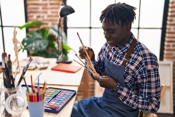 African american man artist smiling confident holding paintbrushes at art studio