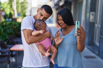 Obraz premium Hispanic family hugging each other having video call at street