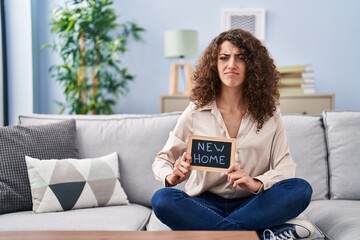 Hispanic woman with curly hair sitting on the sofa at new home skeptic and nervous, frowning upset...