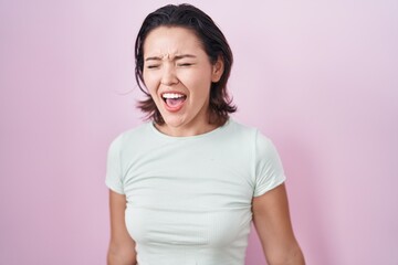 Hispanic young woman standing over pink background angry and mad screaming frustrated and furious,...