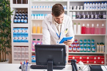 Young caucasian man pharmacist using computer and touchpad at pharmacy