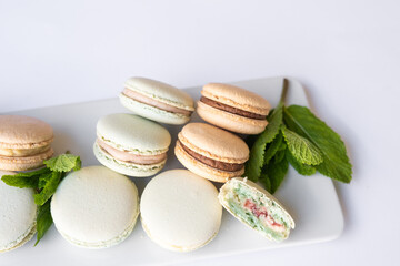 Macaroons of different colors with sprigs of mint on a white background.