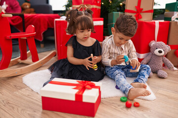 Fototapeta na wymiar Brother and sister playing with toys sitting on floor by christmas gifts at home