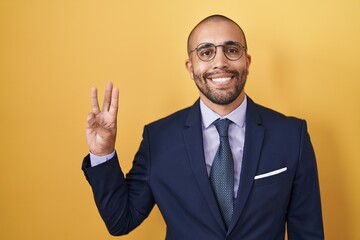 Hispanic man with beard wearing suit and tie showing and pointing up with fingers number three...