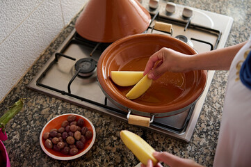 Top view of a housewife cooking tajine, putting slices of organic potato inside a clay dish....
