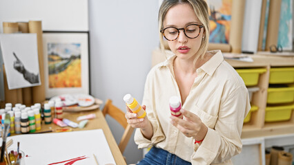 Young blonde woman artist sitting on table choosing color at art studio