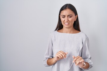 Young hispanic woman standing over white background disgusted expression, displeased and fearful doing disgust face because aversion reaction.