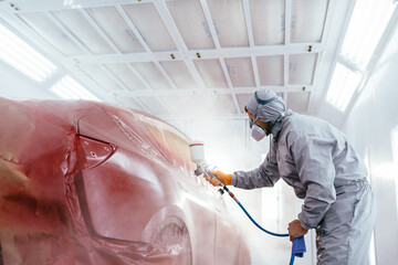 A car service worker coats a car with varnish using compressor. in a special box for painting cars. Automotive paint services, quality auto body shop concept. - obrazy, fototapety, plakaty