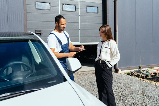 Auto service, repair, maintenance and people concept. Handsome biracial auto mechanic with female client looking at car checklist with bill at auto repair center.