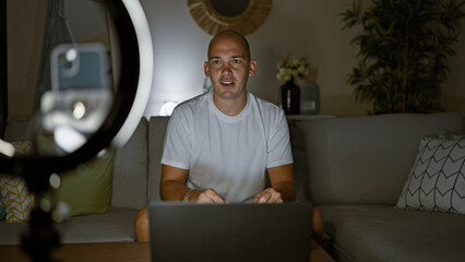 Young hispanic man recording video playing video game sitting on sofa at home