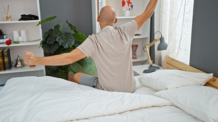 Young hispanic man waking up stretching arms at bedroom