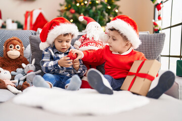 Fototapeta na wymiar Two kids holding gift sitting on sofa by christmas tree at home