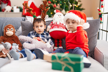 Two kids holding ball sitting on sofa by christmas tree at home