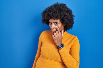 Fototapeta na wymiar Black woman with curly hair standing over blue background pointing to the eye watching you gesture, suspicious expression