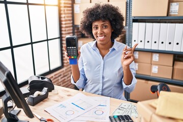 Black woman with curly hair working at small business ecommerce holding credit card and dataphone...