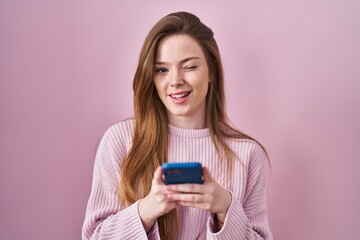 Young caucasian woman using smartphone typing message winking looking at the camera with sexy...