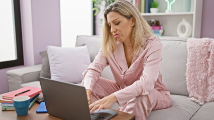 Young blonde woman using laptop with serious face at home