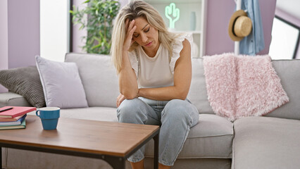 Young blonde woman sitting on sofa stressed at home