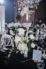 Festive decor with flower composition, candles on black tablecloth. Banquet decoration in hall restaurant. Wedding setup, dinner table reception in area on party. Setting. Birthday, baptism, event.