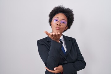 Beautiful african woman with curly hair wearing business jacket and glasses looking at the camera blowing a kiss with hand on air being lovely and sexy. love expression.