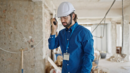 Young hispanic man architect talking on walkie-talkie at construction site