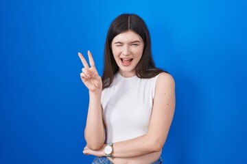 Young caucasian woman standing over blue background smiling with happy face winking at the camera...