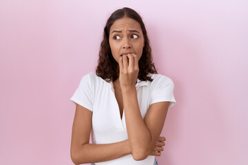 Young hispanic woman wearing casual white t shirt looking stressed and nervous with hands on mouth biting nails. anxiety problem.