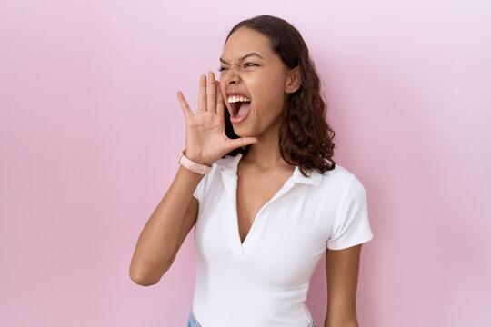 Young hispanic woman wearing casual white t shirt shouting and screaming loud to side with hand on mouth. communication concept.
