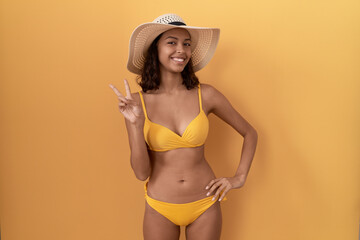 Young hispanic woman wearing bikini and summer hat smiling with happy face winking at the camera...