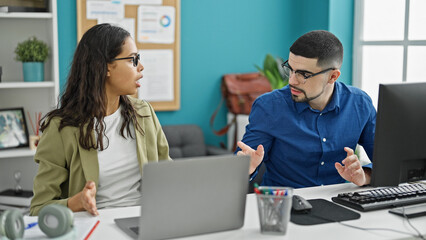 Two office workers, a man and woman, sitting at a table, entangled in a heated argument at their...