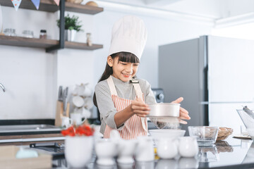 Little asian girl with chef hat and apron cooking in kitchen for homemade bake cake at home