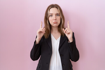 Young caucasian business woman wearing black jacket pointing up looking sad and upset, indicating direction with fingers, unhappy and depressed. - obrazy, fototapety, plakaty